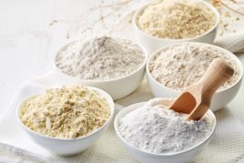 Bowls of various gluten free flour (chick peas, rice, buckwheat, amaranth seeds, almond) on white wooden background
